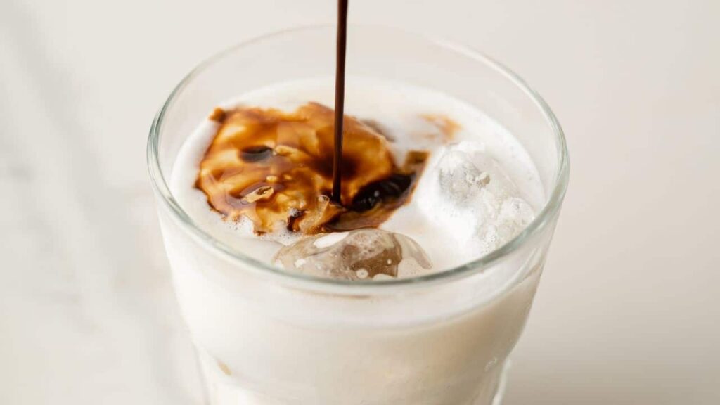 Espresso being poured into glass with milk and ice