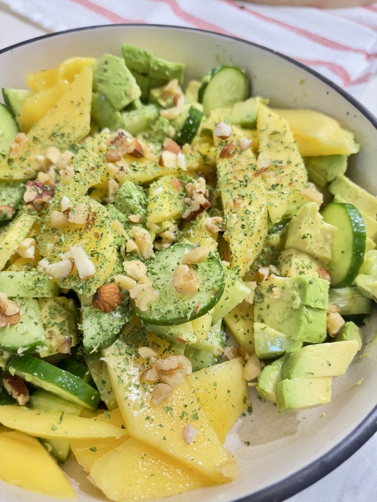 Mango, cucumber and avocado salad in cream bowl, topped with greens and chopped nuts