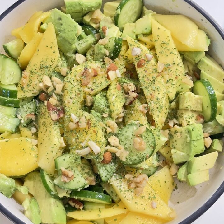 Top down shot of Mango, cucumber and avocado salad in cream bowl, topped with greens and chopped nuts