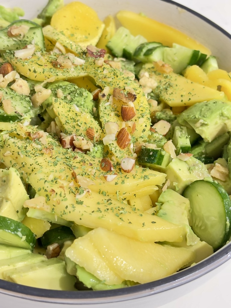 Close up shot of Mango, cucumber and avocado salad in cream bowl, topped with greens and chopped nuts