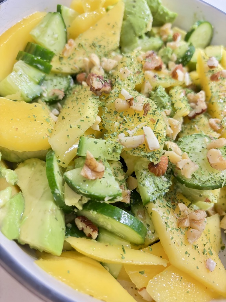 Close up shot of Mango, cucumber and avocado salad in cream bowl, topped with greens and chopped nuts