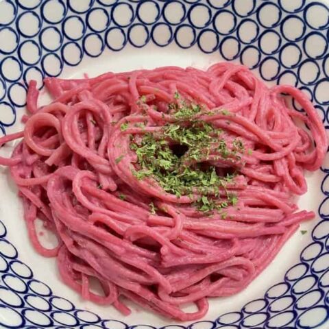 Blue and white bowl filled with pink spaghetti, topped with dried herbs