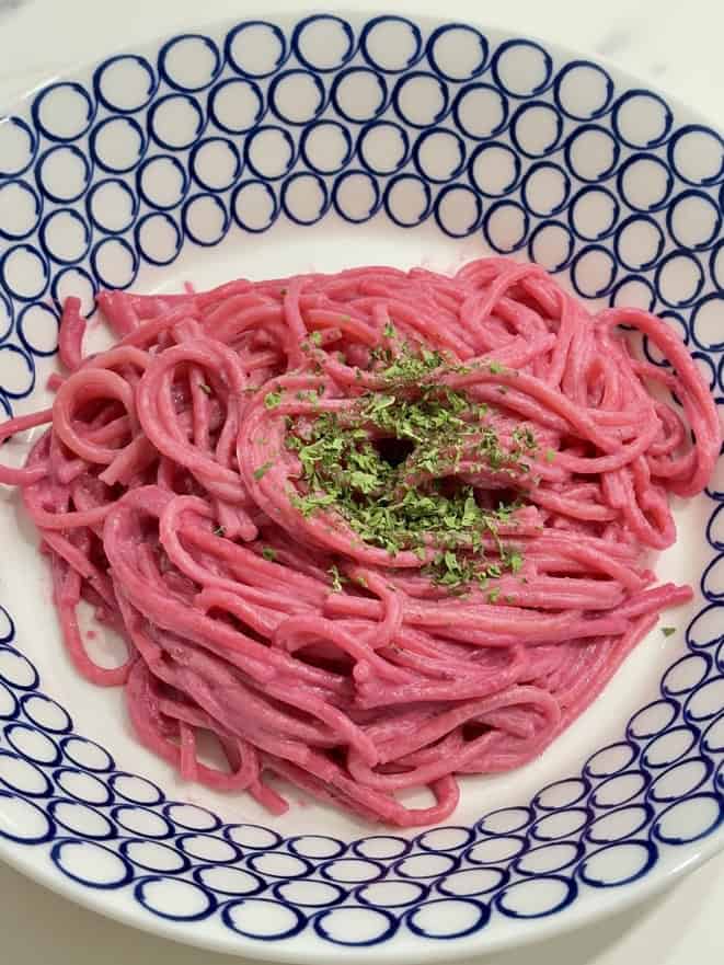 Blue and white bowl filled with pink spaghetti, topped with dried herbs