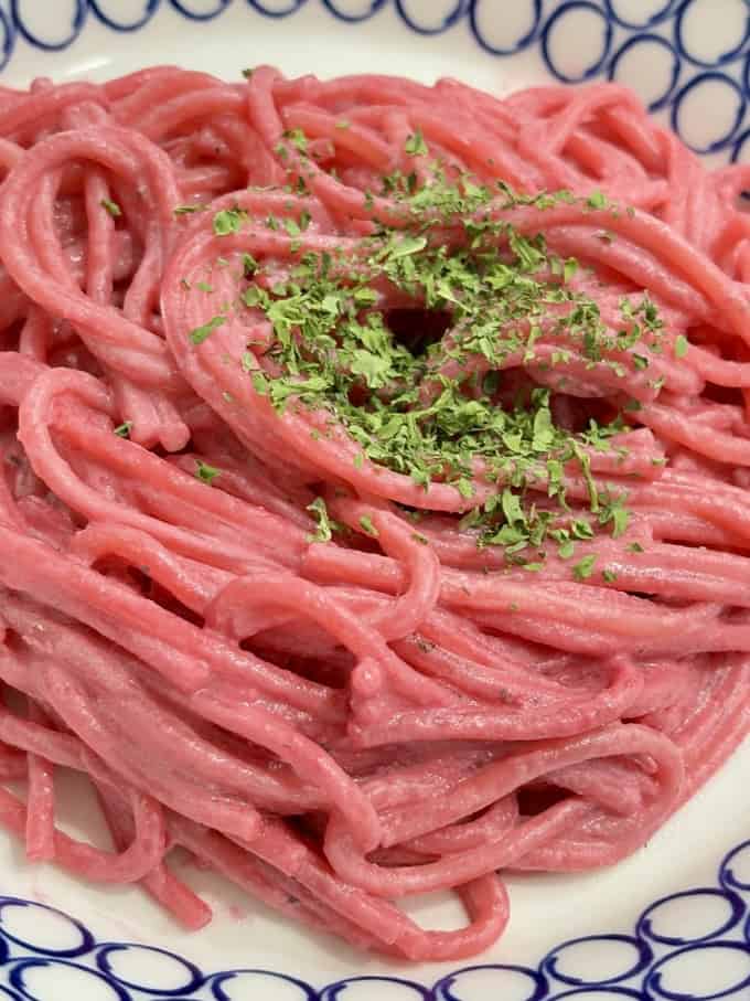 Close up shot of blue and white bowl filled with pink spaghetti, topped with dried herbs