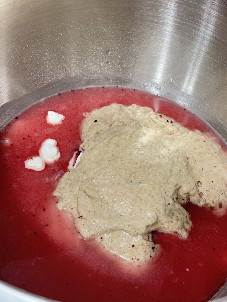 Dough surrounded by pink water in silver bowl