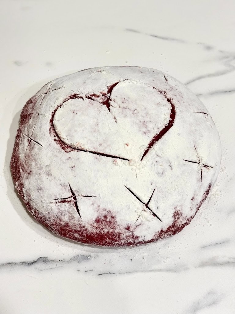 Pink bread dough shaped to loaf, with love heart and x shapes cut into it