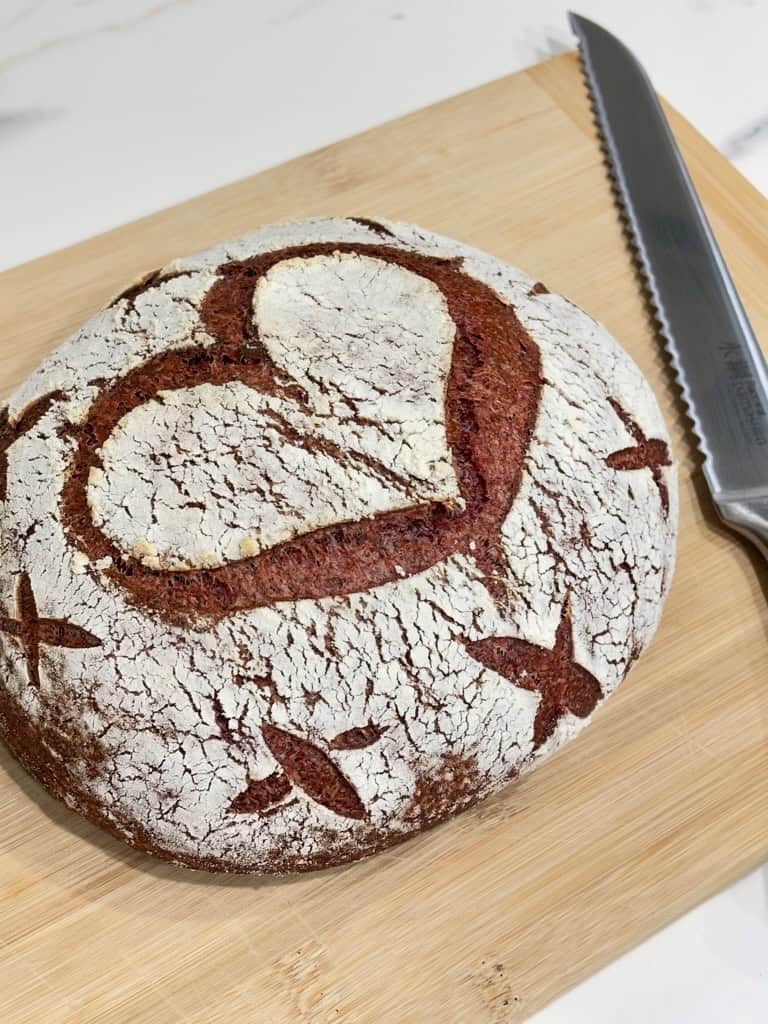 Pink sourdough loaf decorated with heart and x shapes on wooden board