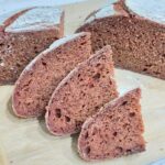 Pink loaf of bread, cut in half, one half sliced, on wooden board