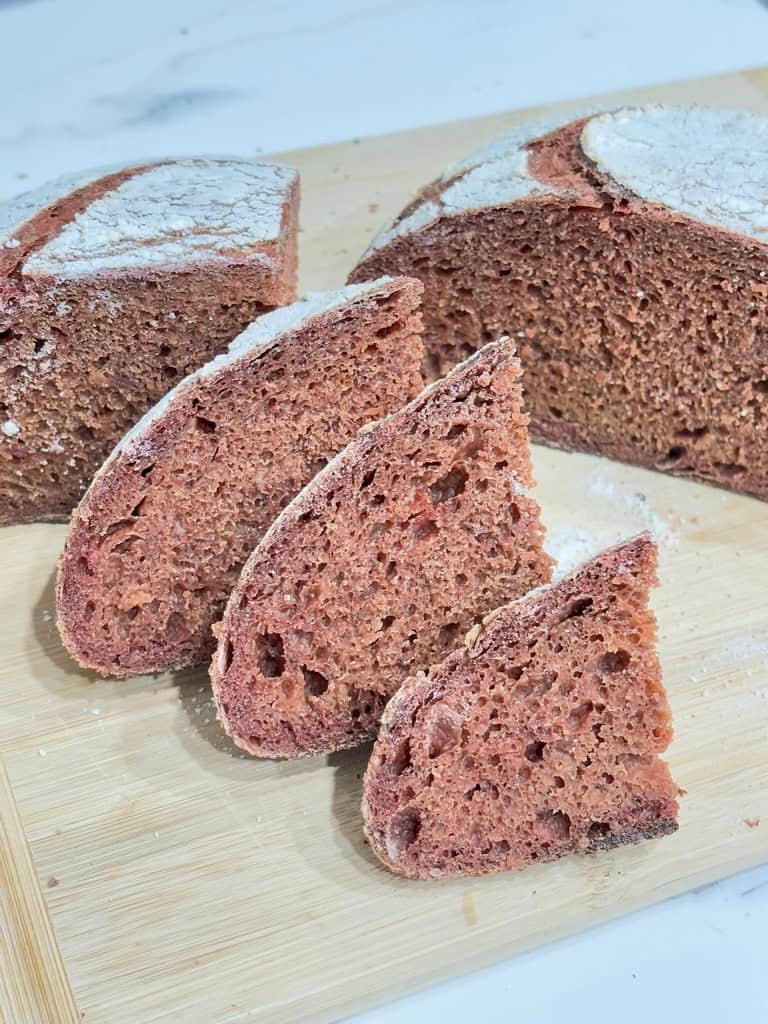 Pink loaf of bread, cut in half, one half sliced, on wooden board