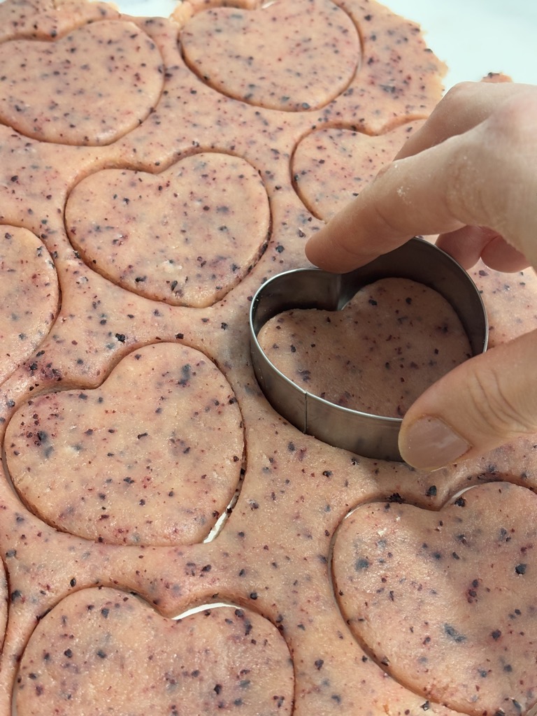 Woman's hand cutting out heart shapes out of pink dough