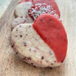 Fanned stack of heart shaped and red decorated cookies on wooden cutting board