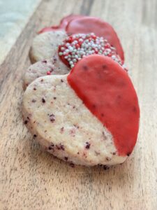 Fanned stack of heart shaped and red decorated cookies on wooden cutting board