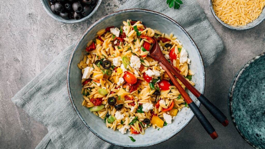 Bowl of colourful pasta salad on linen napkin with wooden serving utensils