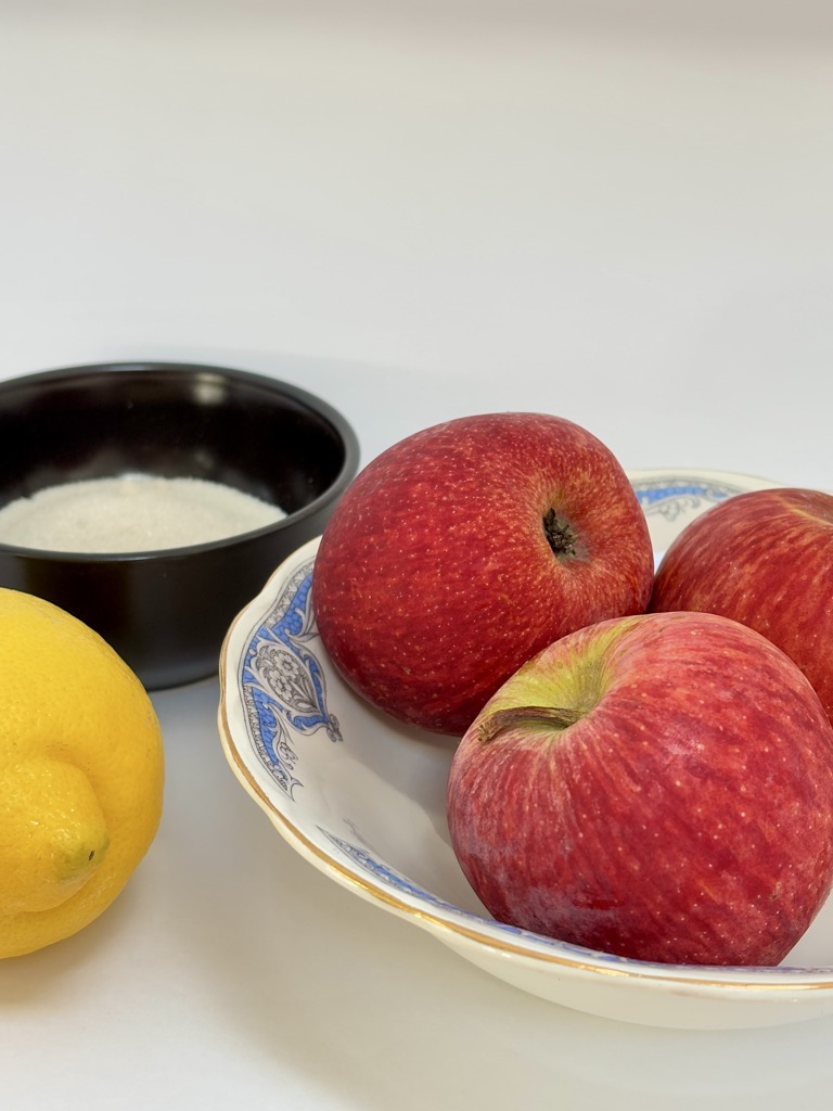 Blue and white vintage bowl filled with red apples next to lemon and black bowl filled with sugar