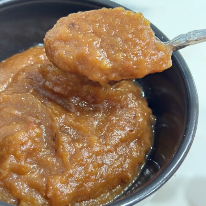 Silver spoon lifting applesauce out of black bowl