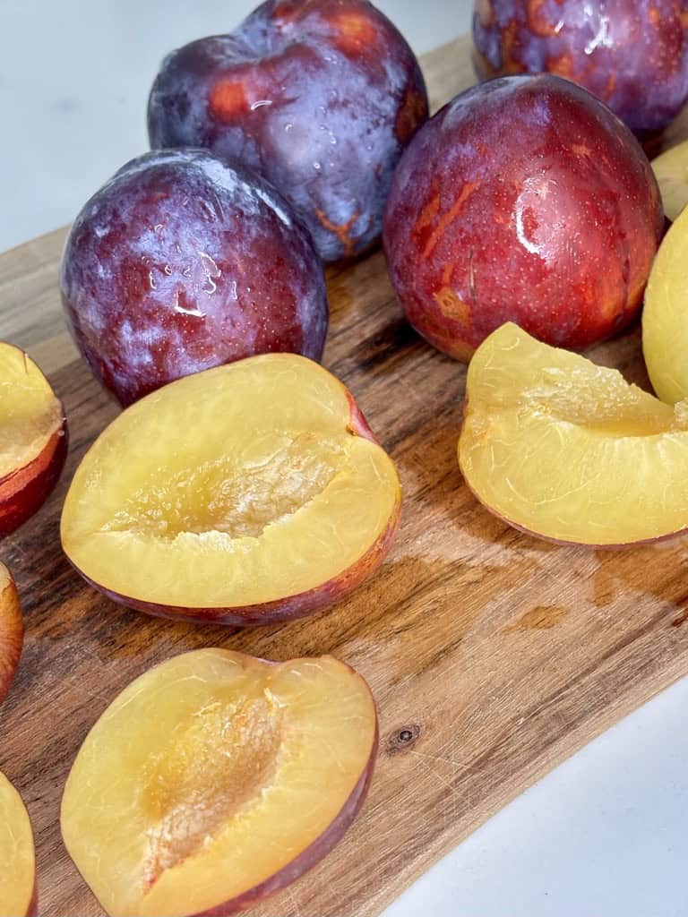 Washed whole and halved plums on wooden board