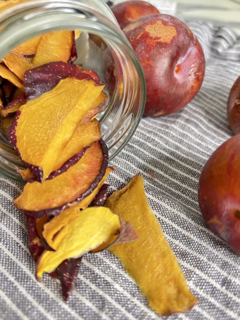 Tipped over glass jar filled with dehydrated plums in front of whole plums