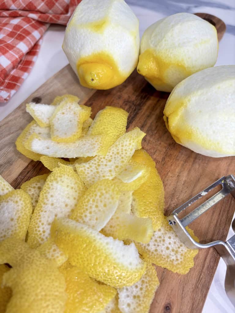 Lemon peel on wooden board with peeler and lemons next to them