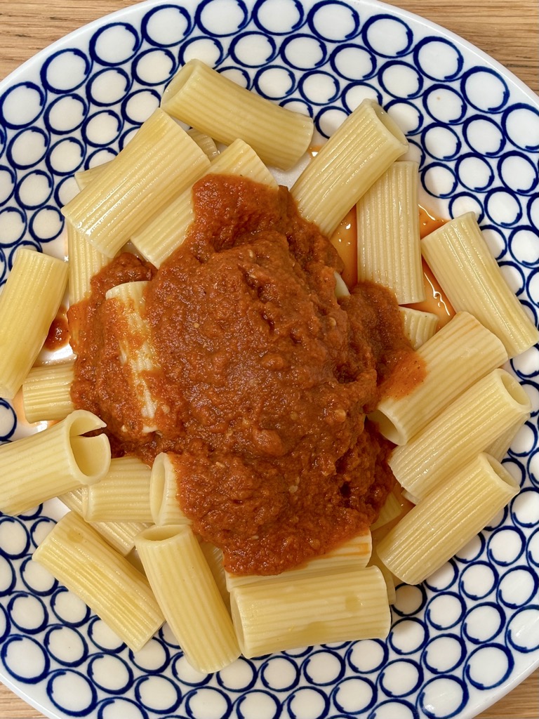 Blue and white bowl of pasta topped with roasted tomato sauce