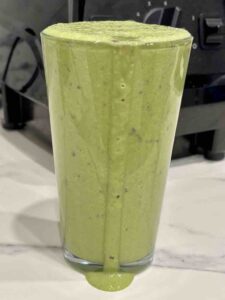 Full glass of green smoothie overflowing onto counter top