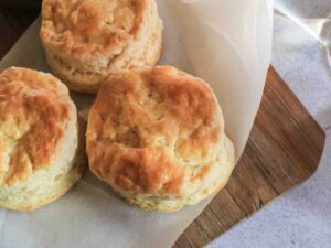Fluffy 3 ingredient scones fresh from the oven, resting on parchment paper over a wooden board – the perfect quick bake for afternoon tea or brunch.