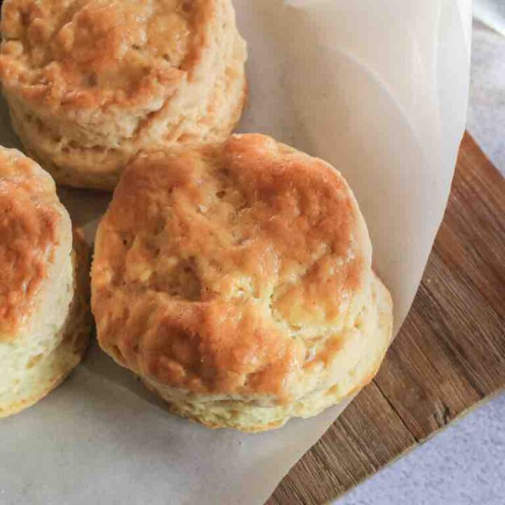 Fluffy 3 ingredient scones fresh from the oven, resting on parchment paper over a wooden board – the perfect quick bake for afternoon tea or brunch.