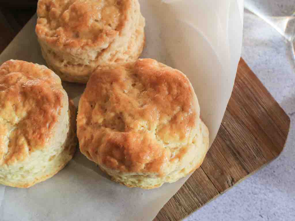 Fluffy 3 ingredient scones fresh from the oven, resting on parchment paper over a wooden board – the perfect quick bake for afternoon tea or brunch.