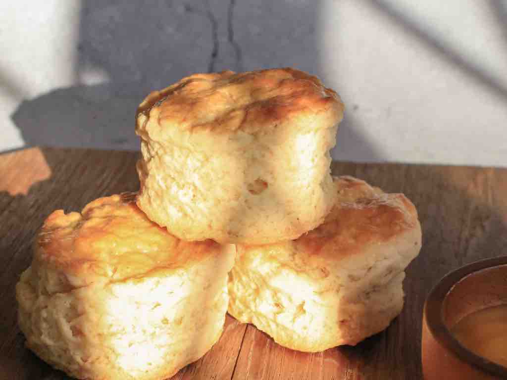 Golden brown 3 ingredient scones stacked on a wooden board, bathed in morning sunlight – an easy and rustic homemade scone recipe idea.