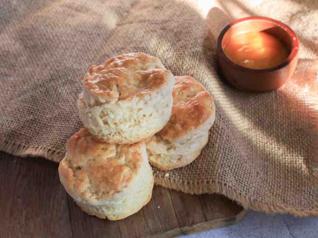 Three golden, freshly baked 3 ingredient scones on a rustic wooden board and hessian cloth, served with a small pot of honey on the side.