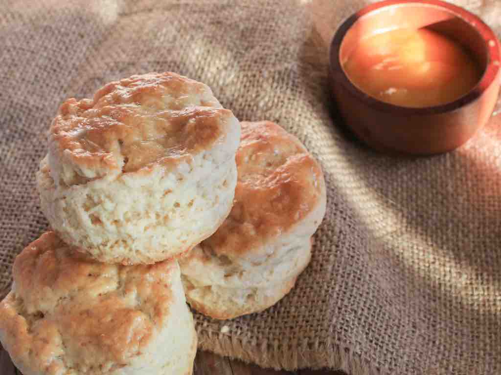 Warm and buttery 3 ingredient scones stacked on a hessian cloth with a wooden bowl of honey – an easy, wholesome treat made from pantry staples.