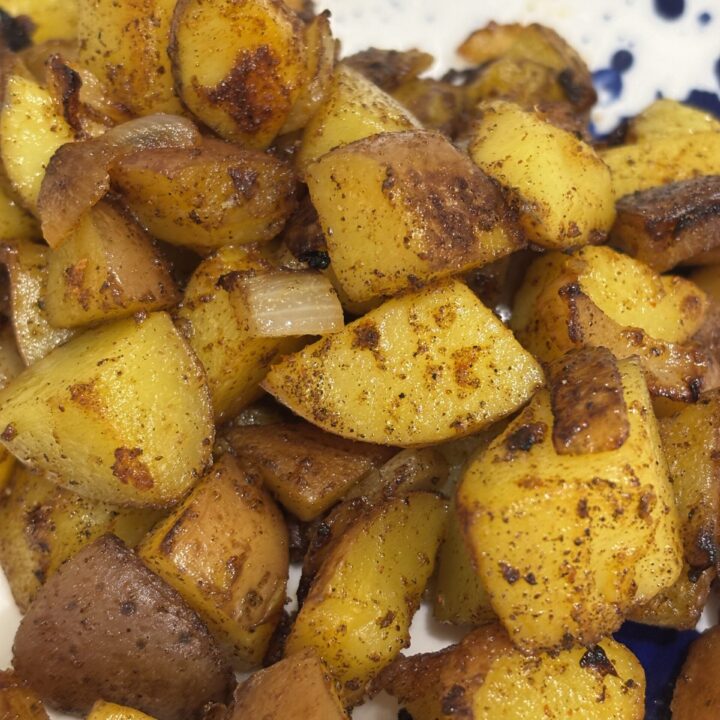 close-up of golden-brown country potatoes, crispy on the outside and tender inside, seasoned with herbs and cracked black pepper, served on a modern white and blue plate