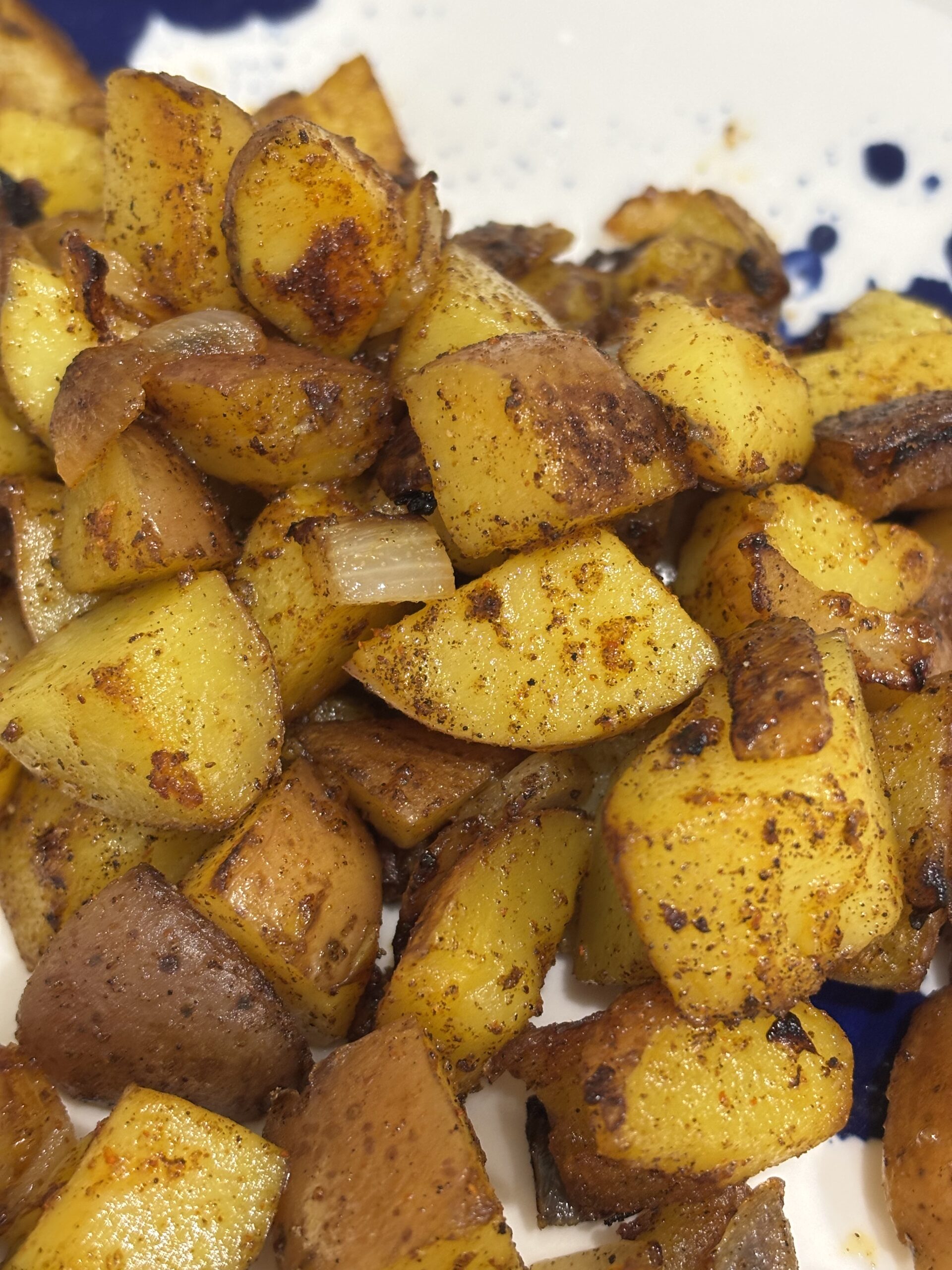 close-up of golden-brown country potatoes, crispy on the outside and tender inside, seasoned with herbs and cracked black pepper, served on a modern white and blue plate