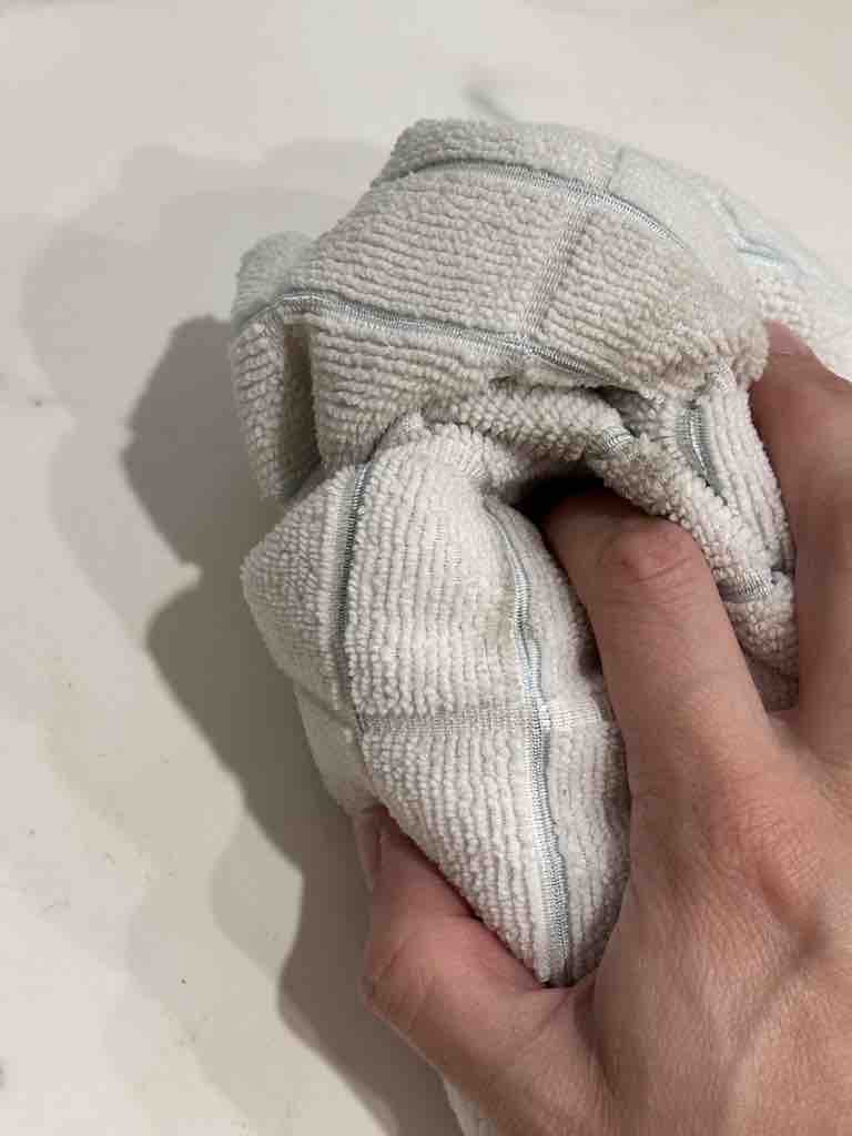 Hand holding a soft microfiber cloth tightly while cleaning, showcasing the scrubbing action of a homemade all-purpose cleaner on a hard surface.