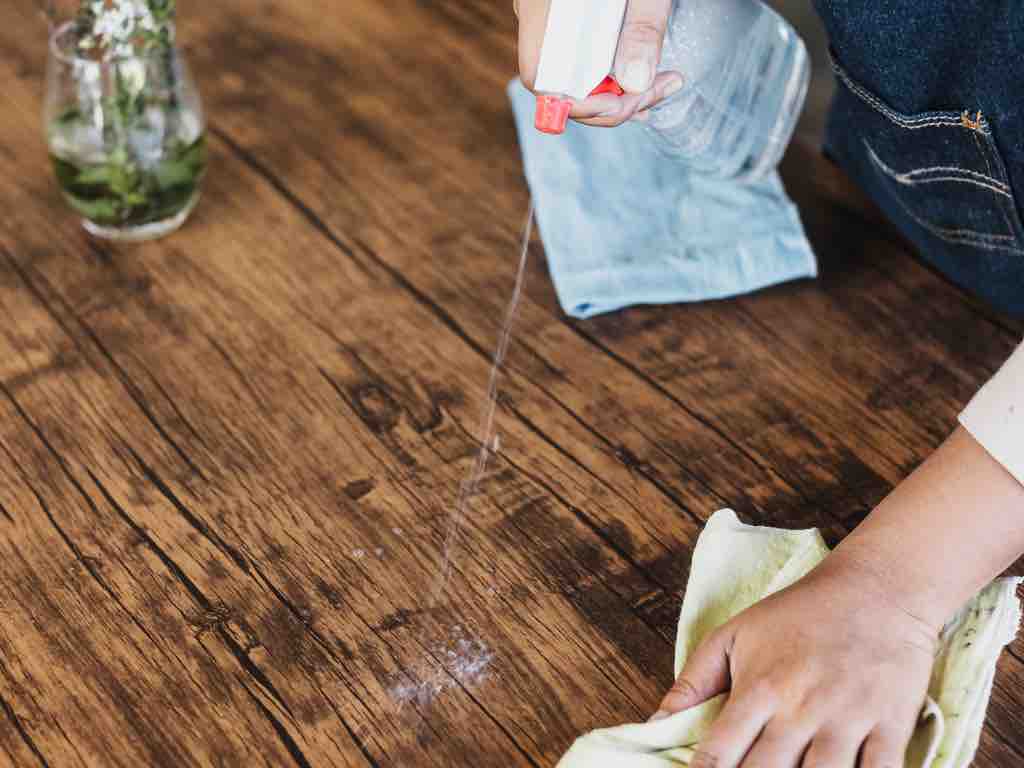 DIY all-purpose cleaner being sprayed on a rustic wooden table, followed by wiping with a cloth—highlighting non-toxic surface cleaning methods.