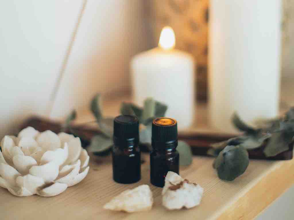 Essential oils, crystals, and a lit candle on a shelf—illustrating the calming, natural elements often added to homemade all-purpose cleaner for scent and wellness benefits.