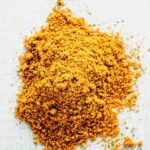 Bright yellow turmeric powder sprinkled loosely on a white surface, highlighting the fine, fluffy texture and rich pigmentation commonly used in cooking and natural remedies.