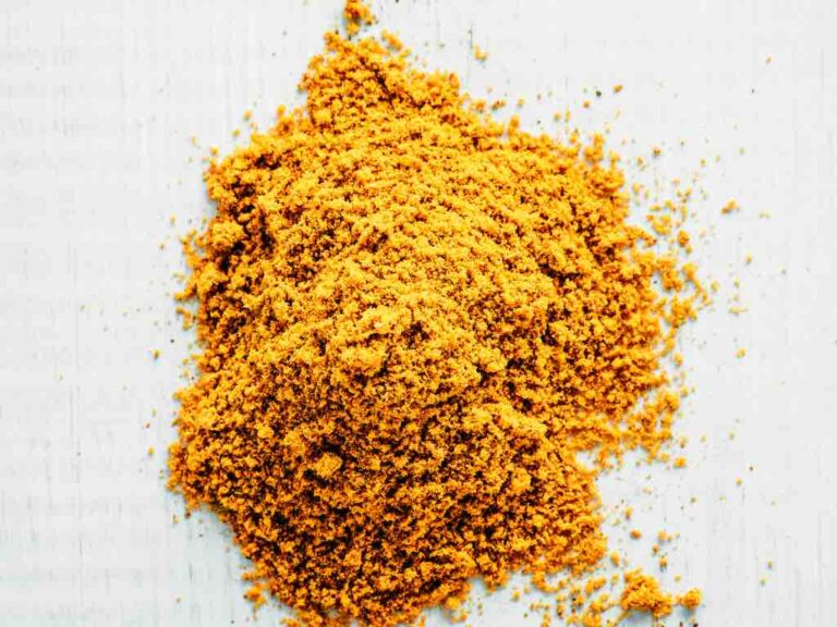 Bright yellow turmeric powder sprinkled loosely on a white surface, highlighting the fine, fluffy texture and rich pigmentation commonly used in cooking and natural remedies.