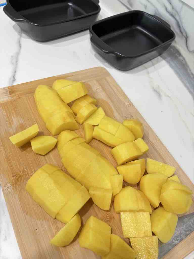 Golden potatoes peeled and roughly chopped on a wooden board, perfectly prepped for a rich and creamy potato gratin or baked potato dish.