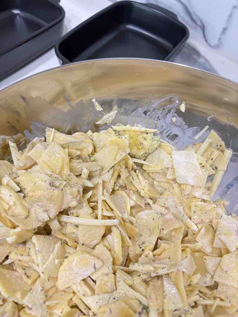 Thinly sliced potatoes tossed in a creamy herb and cheese mixture, ready to be layered into a flavorful potato bake or traditional potato gratin.