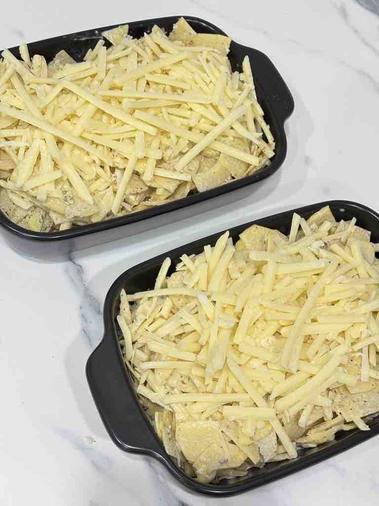 Overhead view of twin baking dishes brimming with layered potato mix and cheese, moments away from turning into a bubbly, cheesy potato bake.