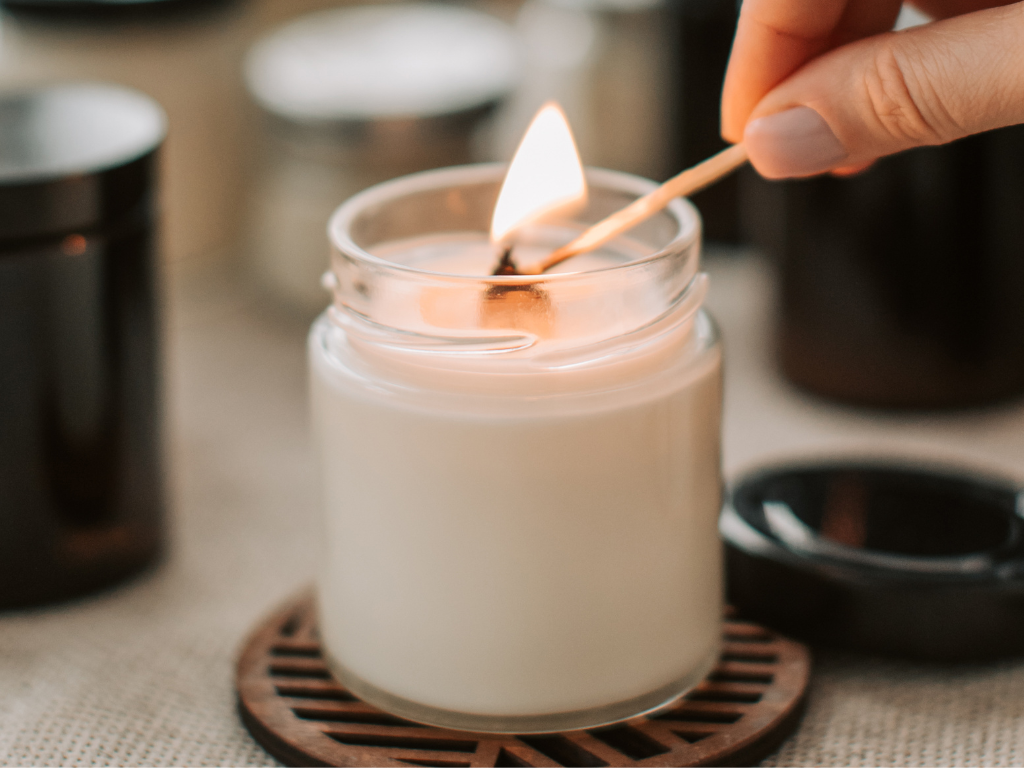 Hand lighting a white candle in a glass jar, a common first step that can sometimes end in wax dripping onto carpeted surfaces.