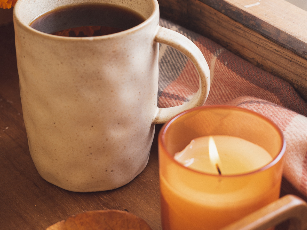 Ceramic mug and glowing candle on a wood tray with a blanket nearby—scenes like this often result in accidental wax on floors and carpets.