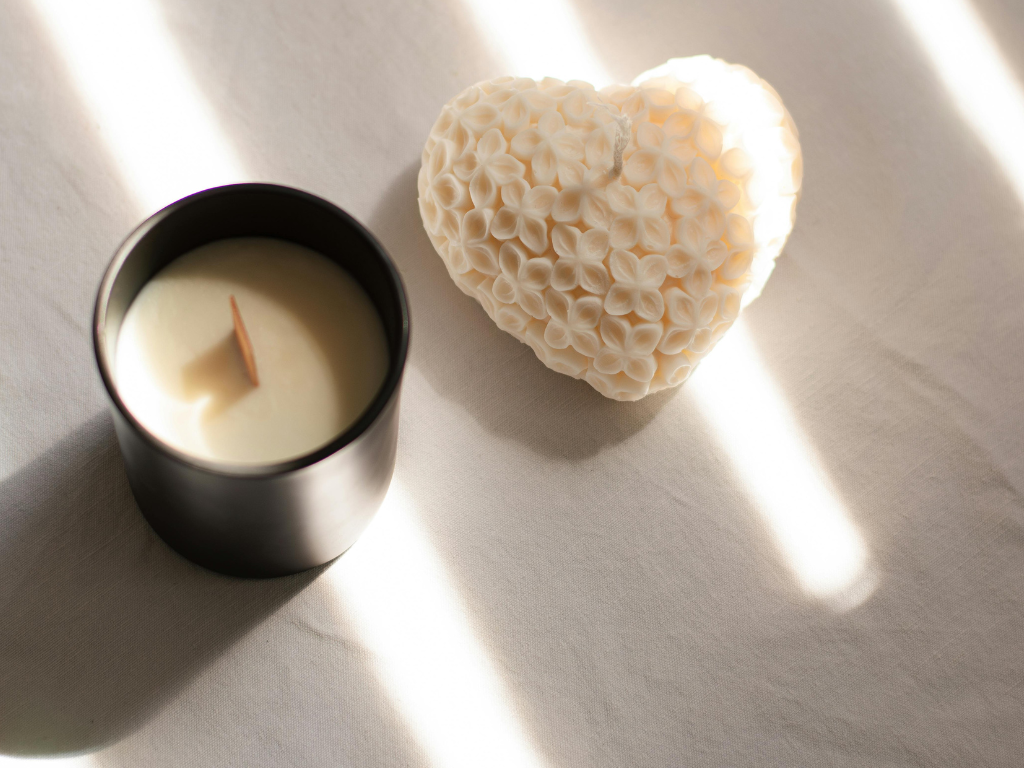 A heart-shaped floral wax candle and modern black jar candle placed on light fabric, demonstrating how wax can melt onto soft surfaces.