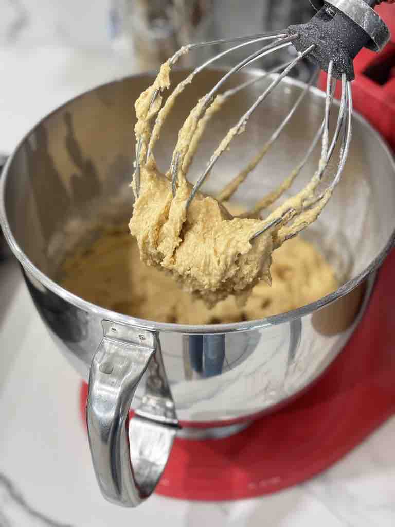 Mixer whisk attachment covered in soft Amerikaner cookie dough, showing the first step in a classic black and white cookies recipe.