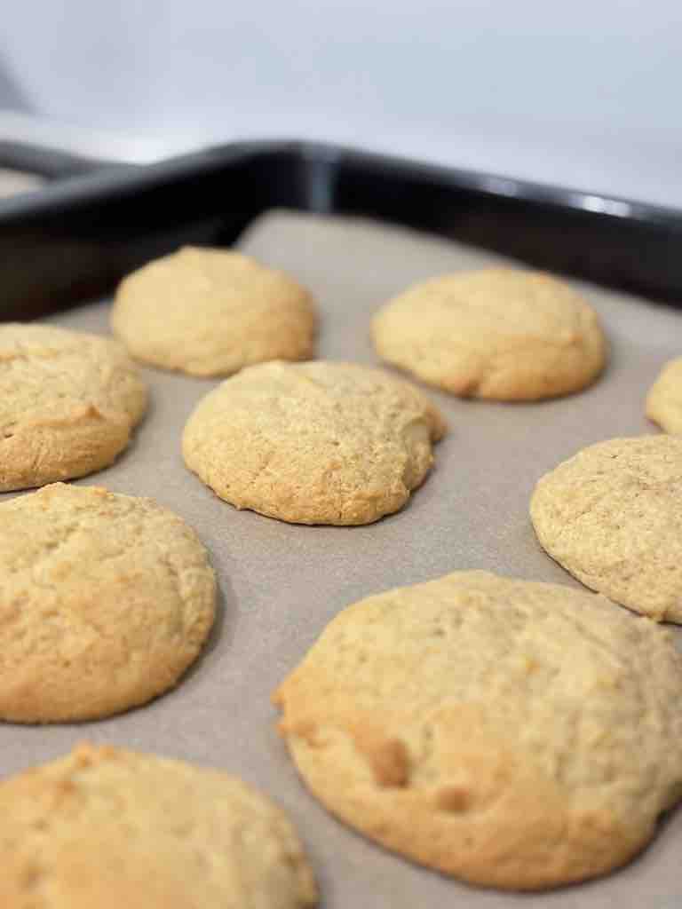 Golden-brown Amerikaner cookies just out of the oven, showing the soft, domed shape perfect for black and white cookie icing.
