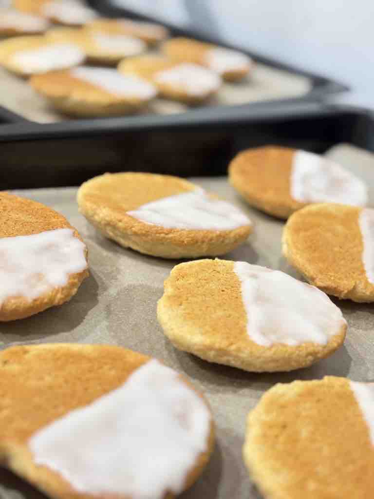 Amerikaner cookies halfway through decorating, with a smooth white sugar glaze covering half of each cookie.