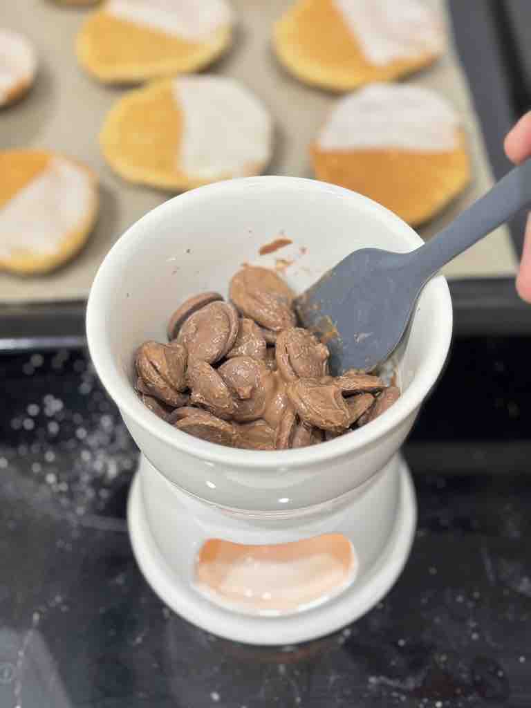 A white fondue pot melting chocolate callets for the second icing layer of homemade Amerikaner cookies.