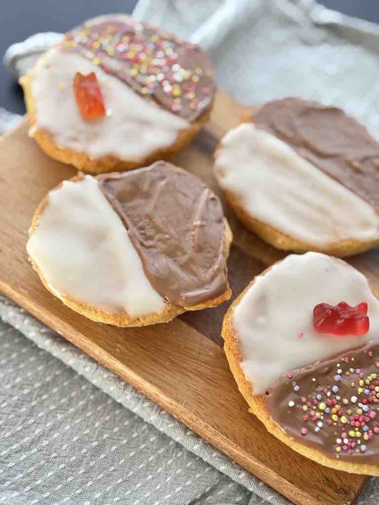Top view of black and white cookies with vibrant decorations including chocolate glaze, white icing, rainbow nonpareils, and gummy bears, served on a rustic wooden board.
