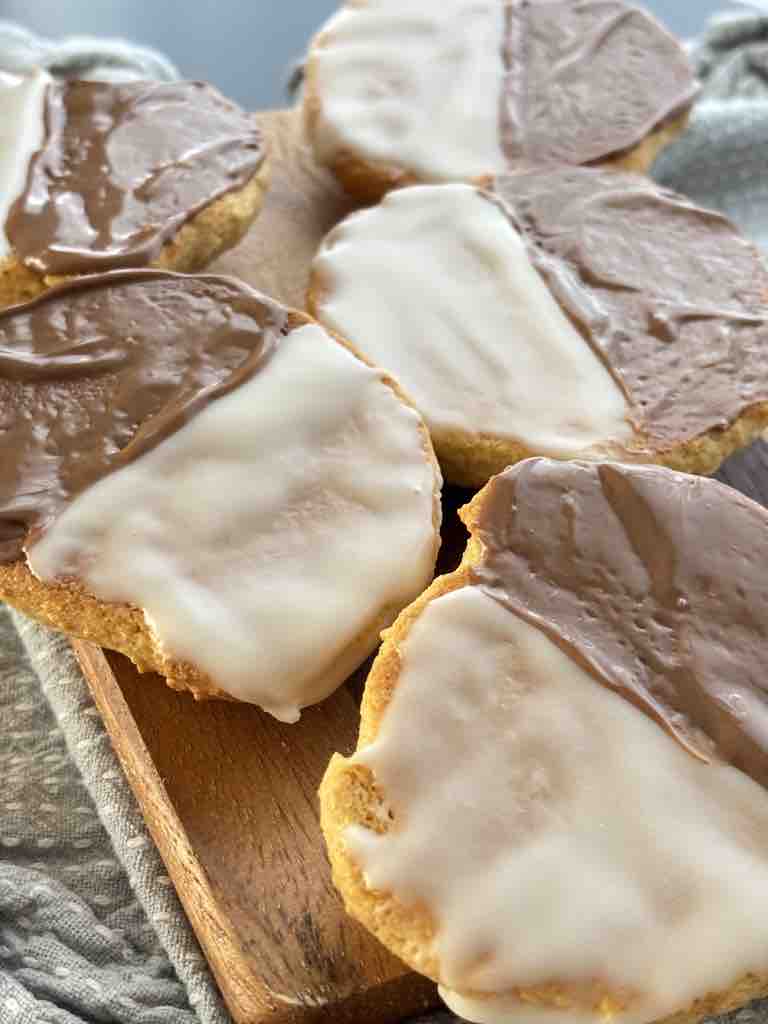 Close-up of classic black and white cookies showing the glossy chocolate and white icing contrast, resting on a rustic board with soft natural light.