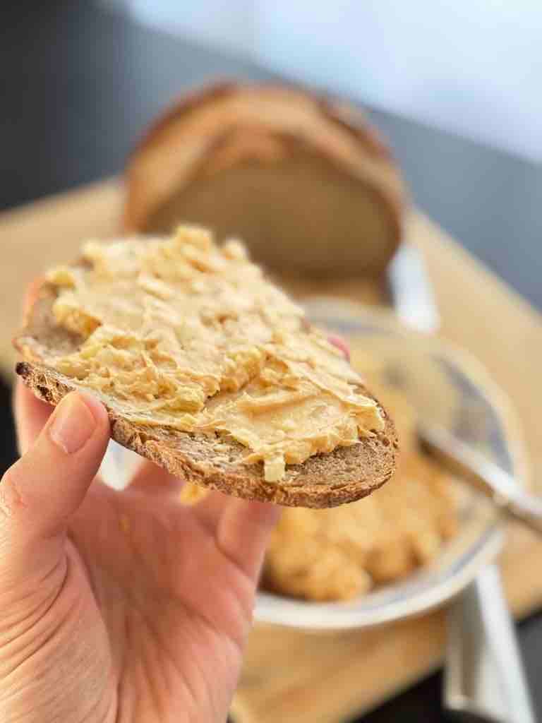 Slice of rye bread spread with creamy German obatzda cheese dip, held in hand.